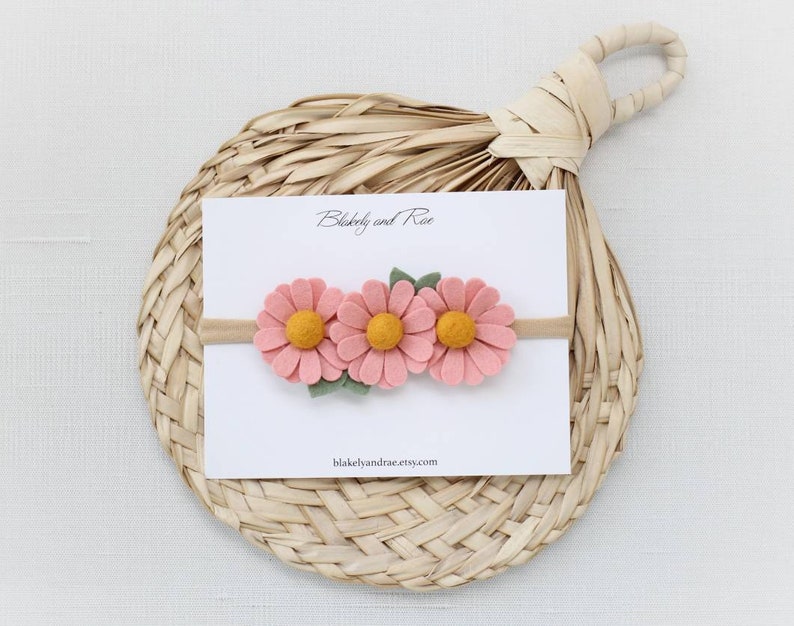 May include: A pink felt flower headband with three flowers and green leaves. The headband is on a white card with the text "Blakely and Rae" and "blakelyandrae.etsy.com".