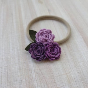 May include: A purple and lavender felt flower headband with three flowers and green leaves.