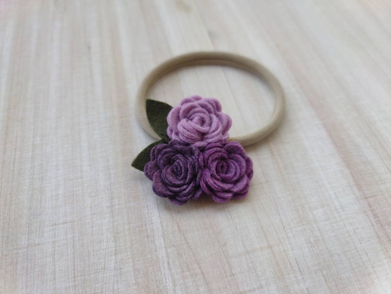 May include: A purple and lavender felt flower headband with three flowers and green leaves.