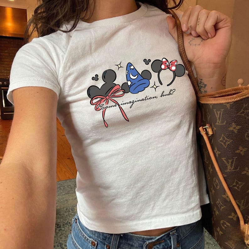 Disney baby tee featuring Mickey and Minnie inspired mouse ears, magic hat and bow design with some imagination huh text for Disney trip outfit