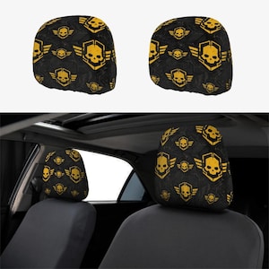 May include: A set of two car headrest covers featuring a repeating pattern of yellow skulls inside hexagonal frames with wings on a black background. The design includes a subtle dark gray circuit board texture across the black fabric surface.
