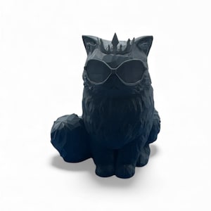 Op de afbeelding: Een donkerblauwe kattenfiguur met zonnebril en kroon. De kat zit rechtop met opgerolde staart. Het beeldje heeft een geometrisch, gesneden ontwerp en staat tegen een witte achtergrond.