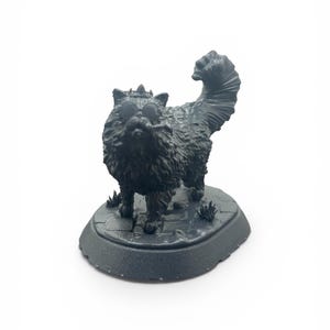 Op de afbeelding: Een donkergrijze kattenfiguur met zonnebril en kroon, staand op een ovale basis met textuur. De kat heeft een pluizig uiterlijk en een gekrulde staart. Het beeldje is een decoratief item.