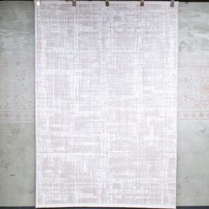May include: A rectangular wall hanging featuring a light beige and white abstract pattern with intersecting vertical and horizontal lines. The fabric is suspended from a black metal rod by four silver metal clips, displaying a textured appearance.