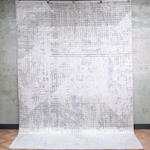May include: A large rectangular area rug featuring a distressed, abstract pattern in shades of white and light grey. The design consists of a grid-like texture with varying densities of grey markings across the surface, creating a faded, weathered appearance.