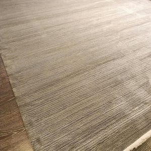 May include: A rectangular area rug in a neutral taupe and grey colour palette. The rug features a textured, linear ribbed pattern running horizontally across the surface. It is finished with short, white fringe detailing along the short edge.