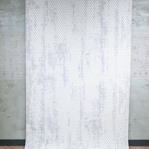 May include: A rectangular curtain panel featuring a light grey and white geometric pattern of small triangles. The fabric displays a distressed, weathered texture with vertical streaks of white across the grey triangular grid design.