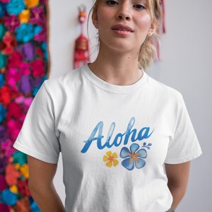 May include: White t-shirt featuring the word "Aloha" in blue script, with yellow and blue floral designs. The shirt is worn by a person.