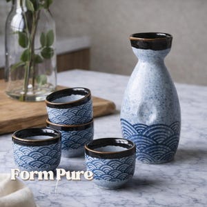 Puede incluir: Un juego de sake de cerámica con una botella y cuatro tazas. El juego tiene un patrón de olas azules y blancas con ribete negro. La botella y las tazas están dispuestas sobre una superficie de mármol. El texto "FormPure" es visible.