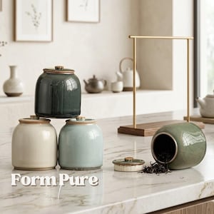 Puede incluir: Conjunto de botes de té de cerámica en varios colores, incluyendo verde, crema y azul, con tapas a juego. Un bote está abierto, revelando hojas de té. Los botes están colocados sobre una encimera.