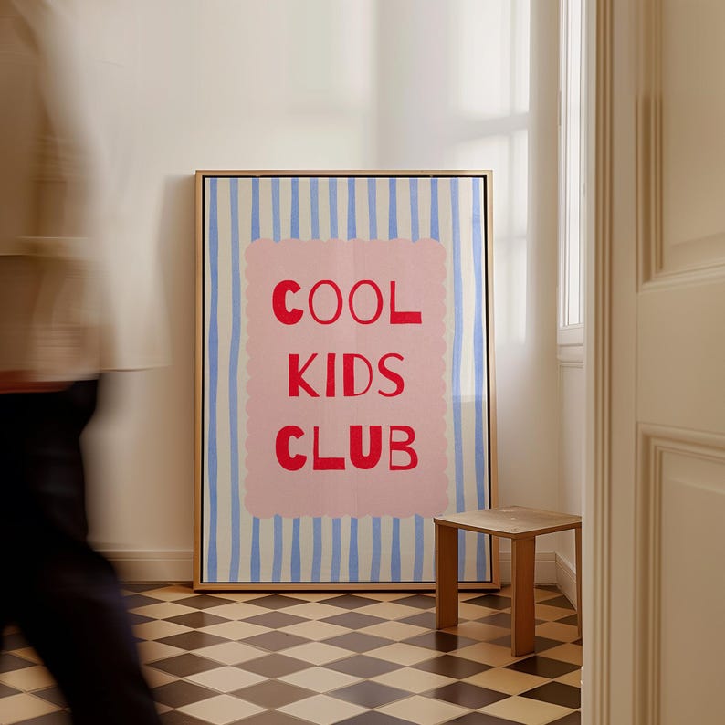 K&ouml;nnte beinhalten: Ein gerahmter Kunstdruck mit dem roten Schriftzug "COOL KIDS CLUB" auf rosa Hintergrund, vor einem Hintergrund aus blau-wei&szlig;en vertikalen Streifen. Das Kunstwerk befindet sich in einem Raum mit einem kleinen Holzschemel und einem Schachbrettboden.