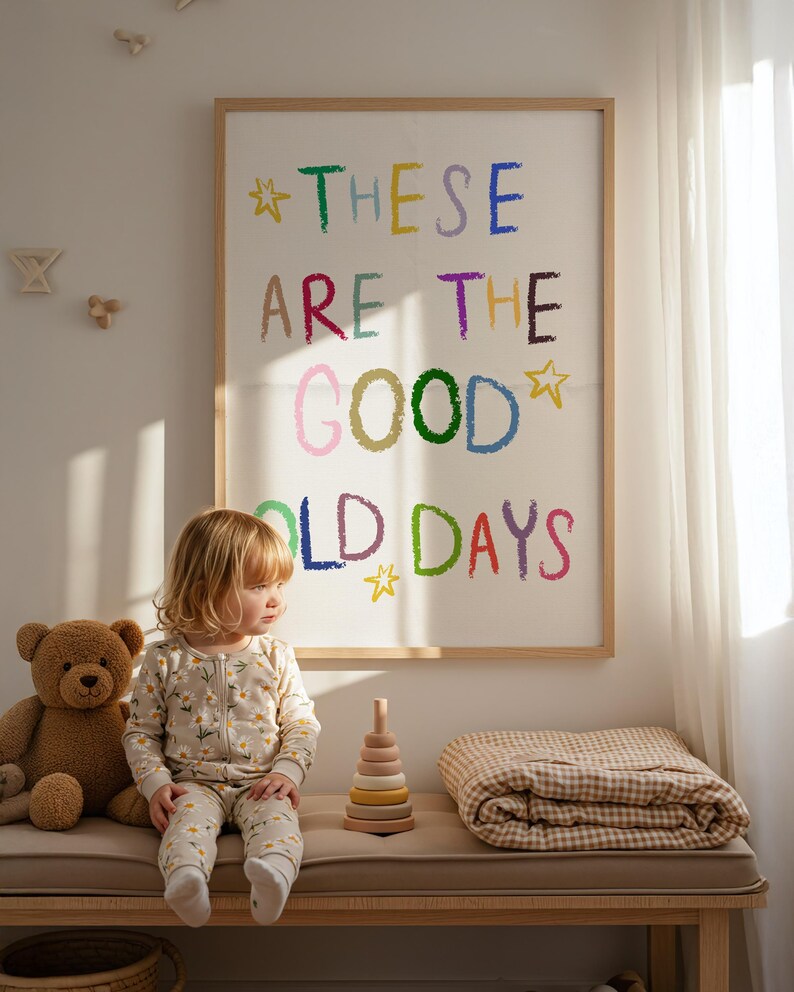 May include: A child in a daisy-print onesie sits on a bench next to a teddy bear and a wooden stacking toy. A framed artwork with the text "THESE ARE THE GOOD OLD DAYS" hangs on the wall.