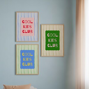 K&ouml;nnte beinhalten: Drei gerahmte Kunstdrucke mit dem Text "COOL KIDS CLUB". Jeder Druck hat ein anderes Farbschema: Rosa und Blau, Gr&uuml;n und Gelb sowie Gr&uuml;n und Beige. Die Rahmen sind hellholzfarben.