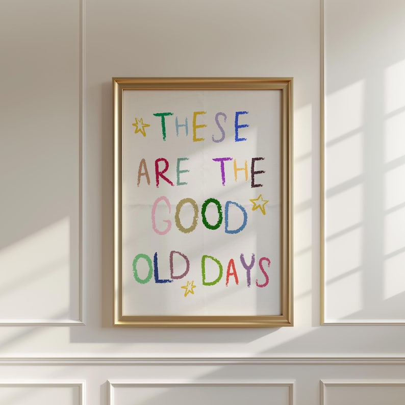 May include: A framed art print with the words "THESE ARE THE GOOD OLD DAYS" in colorful, crayon-style lettering. The text is set against a white background, framed in a gold-colored frame, and accented with star shapes.