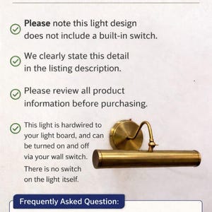 May include: A brass-colored wall-mounted picture light with a cylindrical head and a circular base. The text states: No Switch Included. Please note this light design does not include a built-in switch. This light is hardwired to your light board.
