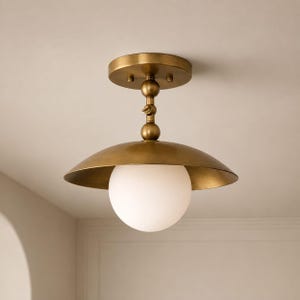 Può includere: Una lampada da soffitto a semi-incasso con una base circolare in ottone e un'asta in ottone abbinata con uno snodo centrale. Un ampio paralume a cupola in ottone circonda una singola lampadina sferica in vetro bianco.
