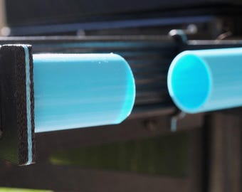 May include: Close-up of two light blue cylindrical objects held in place by black metal brackets. The cylinders have a smooth surface and are evenly spaced. The background is blurred, suggesting an outdoor setting.