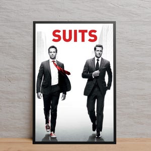 May include: A framed poster featuring two men in suits. The word "SUITS" is in red block letters at the top. One man wears a red tie and red sneakers. The other man wears a black tie and black shoes. The background is a grayscale image of a city.