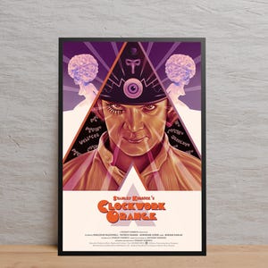 May include: A framed poster for the film "Clockwork Orange." The artwork features a man with a distinctive hat and eye, set against a purple and white backdrop. The title is in orange. The poster is in a black frame.