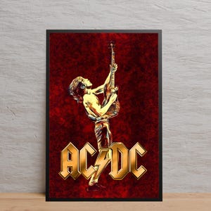May include: Framed art print with a stylized illustration of a guitarist. The image has a red background and gold text reading "AC/DC". The musician is shown in a dynamic pose, holding the guitar aloft. A striking piece of wall art.