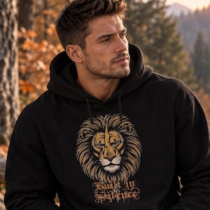 Könnte beinhalten: Ein schwarzer Kapuzenpullover mit einem grafischen Druck eines Löwenkopfes, der einen gelben Blitz auf der Stirn trägt. Unter dem Löwen ist der Text "Built in Silence" in einer stilisierten, abgenutzten Schriftart gedruckt. Der Hoodie hat eine Fronttasche.