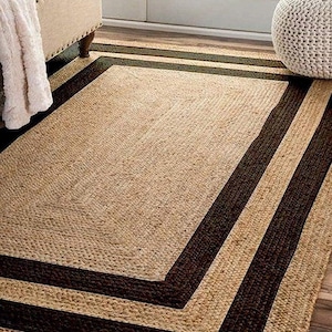 May include: A rectangular jute rug with a dark brown border. The rug has a natural, woven texture and is placed on a hardwood floor. The rug's dimensions are approximately 152 cm by 244 cm.