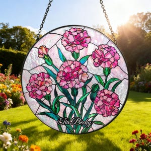 Puede incluir: Vidriera redonda con claveles rosas con hojas y tallos verdes. La obra de arte está enmarcada en negro y cuelga de una cadena. El texto "Tia Becky" está en la parte inferior de la imagen.