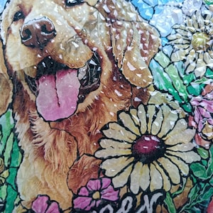 May include: A mosaic artwork featuring a Golden Retriever dog with its tongue out, surrounded by colorful flowers. The artwork has a stained-glass effect, with a black border. The flowers include daisies and other blooms in shades of pink, yellow, and green.