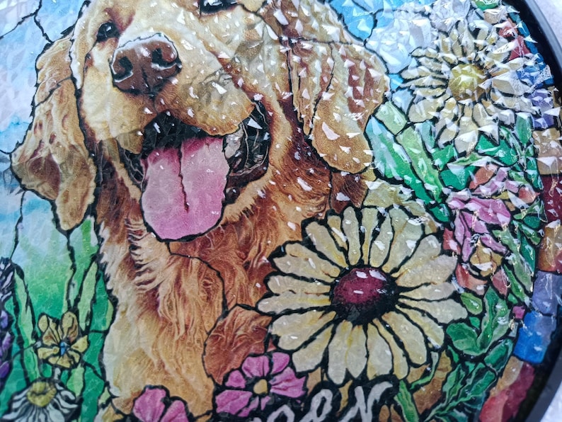 May include: A mosaic artwork featuring a Golden Retriever dog with its tongue out, surrounded by colorful flowers. The artwork has a stained-glass effect, with a black border. The flowers include daisies and other blooms in shades of pink, yellow, and green.