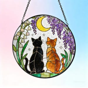 May include: Round stained glass window art featuring two cats, one black and one orange, gazing at a yellow crescent moon. The design includes purple wisteria, white flowers, and stars, with a black chain for hanging.