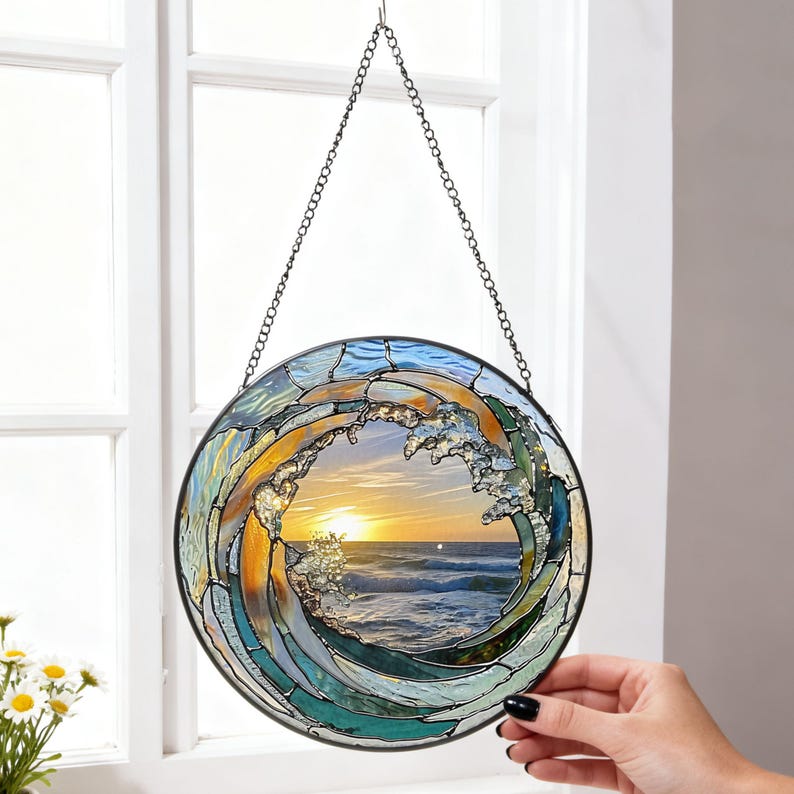 May include: A round stained glass window depicting a wave with a sunset scene. The wave is made of blue, green, and gold glass, with a black metal frame and chain for hanging. The sunset features orange and yellow hues.