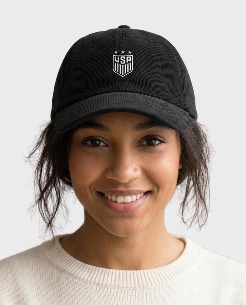 May include: Black corduroy baseball cap featuring the USA emblem in white. The emblem includes three stars above a shield with vertical stripes and the letters "USA". The cap has a curved brim and an adjustable strap.