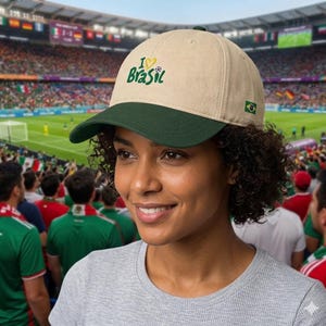 K&ouml;nnte beinhalten: Beige Baseballkappe mit gr&uuml;nem Schirm, mit dem Text "I ❤️ Brasil" und einer brasilianischen Flagge. Die Kappe wird von einer Person in einem Stadion getragen.
