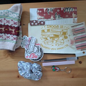 May include: A selection of items including cream socks with a reindeer design, a canvas bag with the text "All I Want For Christmas Is Books", stickers, a scrunchie, a pen, and a Christmas-themed keychain.