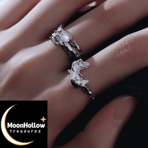 May include: Two silver rings with a moon and star design. The rings have a textured, dark metal band with a crescent moon and a star-like embellishment. The rings are worn on a hand, with the MoonHollow treasures logo in the bottom left corner.