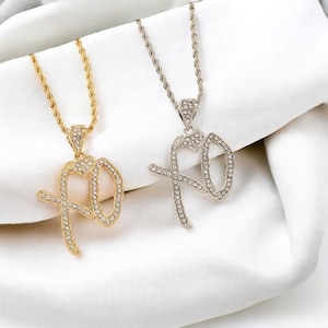 May include: Two necklaces with pendants spelling "XO" in a cursive font, encrusted with small, clear crystals. One necklace is gold-toned, the other silver-toned, both with rope chains. The pendants feature a heart-shaped design.