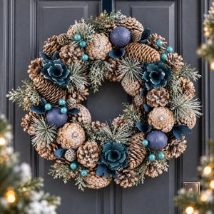 May include: A circular wreath featuring brown pinecones, frosted evergreen sprigs, dark blue matte spheres, and teal-coloured decorative flowers. The arrangement is densely packed with natural textures and cool-toned accents, creating a winter-inspired display suitable for hanging on a door or wall.