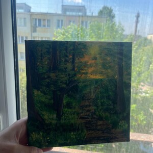 Op de afbeelding: Een vierkant canvas schilderij met een bossc&egrave;ne en een zandpad dat door donkergroene bomen slingert. Het kunstwerk toont een heldere gele en oranje gloed die door het bladerdak filtert, wat zonlicht suggereert, met diepe schaduwen en texturen.