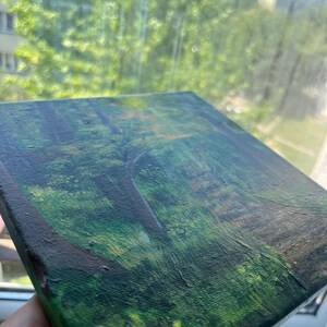 Op de afbeelding: Een vierkant canvas schilderij met een boslandschap met diepgroen gebladerte, donkerbruine boomstammen en gevlekt licht dat door het bladerdak filtert. De textuur van de verf zorgt voor een gelaagd effect op het oppervlak van het kunstwerk.