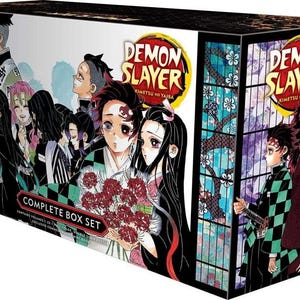 Op de afbeelding: Een complete boxset van de mangaserie "Demon Slayer: Kimetsu no Yaiba". De doos bevat kleurrijke illustraties van personages uit de serie, waaronder Tanjiro Kamado en Nezuko Kamado. De boxset bevat meerdere volumes van de manga.