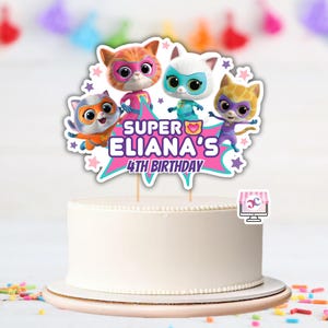 May include: A white iced cake with a decorative topper featuring four cartoon superhero cats. The topper reads "SUPER ELIANA'S 4TH BIRTHDAY" in pink and blue. Colourful confetti and a banner are in the background.