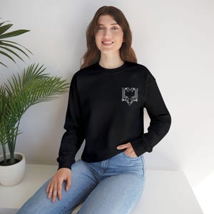 May include: Black sweatshirt featuring a white, detailed emblem of a double-headed eagle on the chest. The long-sleeved top is paired with blue jeans. The eagle design is a prominent feature, adding a touch of national pride.