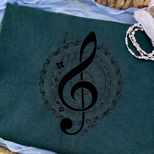 Peut inclure: Cahier bleu canard foncé avec un motif de clé de sol noire dans un cadre circulaire décoratif. Le symbole musical est centré sur le cahier, entouré d'un panier tressé et de tissu bleu.