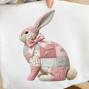 Peut inclure: Un lapin décoratif en patchwork avec des carrés de tissu roses, floraux et bleu clair. Le lapin a de longues oreilles à pois, un nœud rose et une queue blanche duveteuse. Un objet décoratif de Pâques.