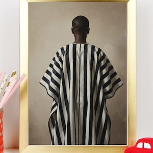 May include: A framed art print depicting a person from the back, wearing a black and white striped garment. The artwork is set against a neutral background and framed in a gold-coloured frame. The print has a minimalist aesthetic.