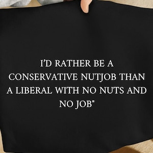 May include: Black fabric with the white text: "I'D RATHER BE A CONSERVATIVE NUTJOB THAN A LIBERAL WITH NO NUTS AND NO JOB". The fabric is held by a person.