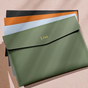 May include: Four leather document holders in a layered arrangement. The colours are olive green, light blue, orange, and black. The olive green holder has the name "Lisa" embossed in gold. The holders are designed to store documents and papers.