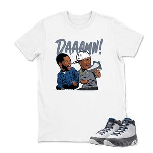 May include: White t-shirt featuring a cartoon graphic of two men with the word "DAAAMN!" above them. The men are looking at a sneaker. A pair of gray and white sneakers with navy blue accents are at the bottom of the image.