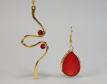 Pendientes asimétricos hechos a mano chapados en oro, con cristales Swarovski rojos en forma de lágrima y diseño de ondas fluidas.