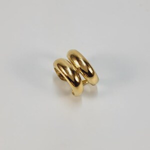 May include: A pair of gold-colored hoop earrings. The earrings have a double-hoop design, with two connected, rounded hoops. The earrings are made of a shiny, reflective metal, and are set against a white background.